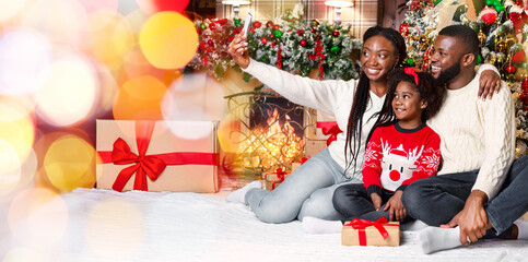 Festive selfie. Happy afro woman taking photo with her husband and daughter in decorated living room near Christmas tree and fireplace