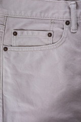 Close-up of a beige denim jeans pocket with a leather jacket detail on white background