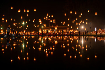 Fire Lanterns Floating up into the sky is reflection in the water at night at Loi Krathong Festival Travel Destinations Of Chiang Mai, Thailand.