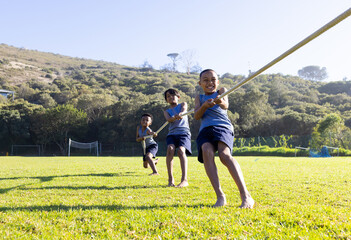 Naklejka premium Playing tug of war, three multiracial boys having fun outdoors at school field