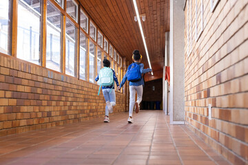 Running in school hallway, two african american girls with backpacks holding hands