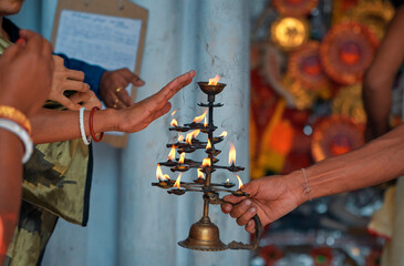 devotees taking the warmth of burning diyas (holy flame of religious offering) from hindu priest,...