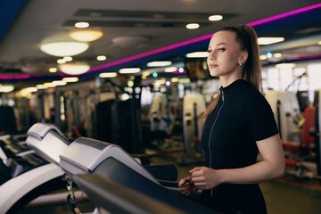 Naklejka premium Young woman exercising on treadmill in modern gym during daylight hours