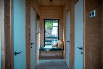 A cozy wooden hallway with natural light illuminating a seating area surrounded by three doors in a serene cabin setting