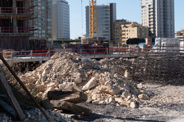 Building site of a new apartment under construction. Rubble in foreground, with cranes and steel mesh next to a large hole where the foundations are being laid.