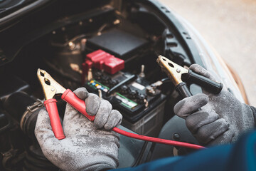 Obraz premium Car mechanic holding connect jumper cable or car booster cables on terminal dead battery for jump-start or check car battery fail problem change repairing and fix car with maintenance service.