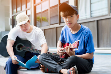 Asian teens sitting and practicing acoustic guitar playing together, soft focus, lifestyles of young people concept.