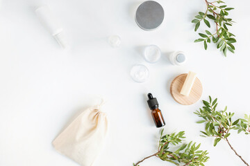 Overhead view of blank cosmetic bottles, brown glass cosmetic dropper bottle for face serum or oil, pistachio branches, linen bag on a white background. Face care routine.