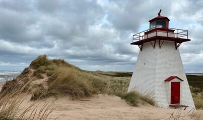 St. Peters Harbour Lighthouse stands on a sandy dune with beach grass under a cloudy sky