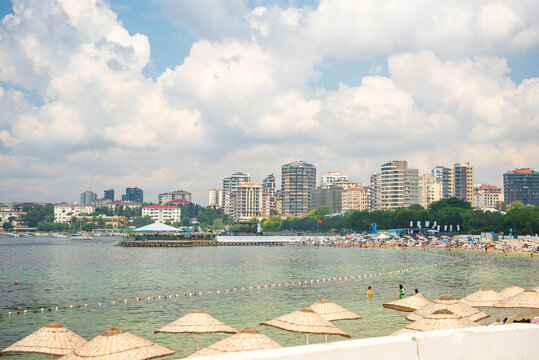 Istanbul, Turkey - July 7, 2024: People resting on the Caddebostan sandy beach. Citizens swimming and sunbathing under umbrellas on summer sunny day. Asian side of Istanbul city in the background