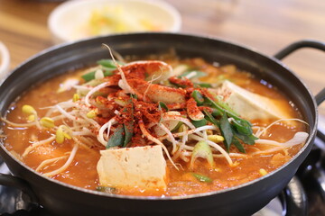 A steaming bowl of rich, flavorful kimchi stew with bean sprouts, topped with a sprinkle of red pepper flakes. The vibrant colors and hearty ingredients showcase a classic Korean dish.