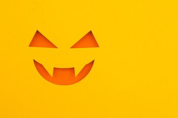 A simple orange and yellow paper cutout of a jack-o'-lantern face on a bright yellow background