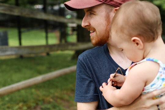 Father in red baseball hat holding infant daughter in the park