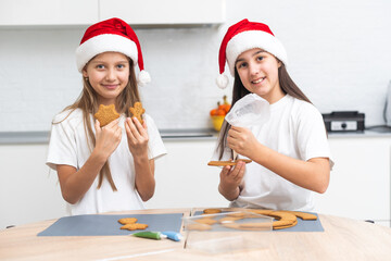 Children are cooking Christmas cookies in cozy home kitchen. Cute kids in santa hats preparation holiday dinner for family. sisters bake Xmas biscuits. Lifestyle moment. Children chef concept.