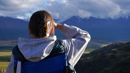 Fototapeta premium Back view of faceless girl in casual clothes standing alone on green hill and enjoying picturesque view of mountains