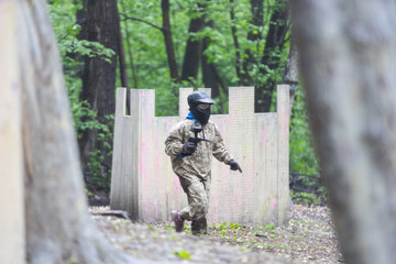 Fototapeta premium Paintball game. Players with weapons shooting paint balls. Men on the playground. Guys in camouflage and masks are fighting.
