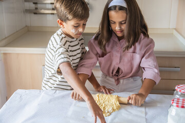 Happy Boy And Girl Aged Nine Kneading Dough For Homemade Cookies In The Kitchen With Smiles And Positive Emotion As Little Chefs