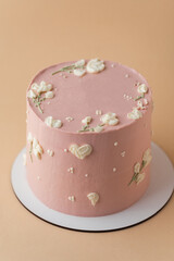 Beautiful birthday cake with peach color chocolate icing on the beige pastel background decorated with cream flowers