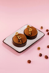Chocolate tarts covered with chocolate velour and topping with sliced nuts isolated on plate with pink background.