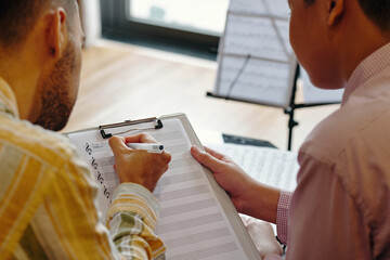 Colleagues discussing musical notes on a clipboard during a work session in an office setting....