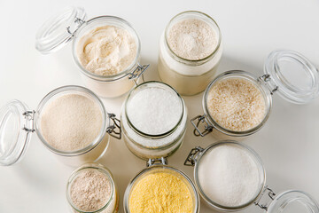 food storage, culinary and eating concept - close up of jars with different kind of flour, salt and sugar on white background, top view