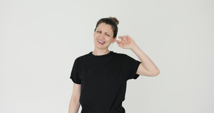 Woman suffers from pain in ear and winces in discomfort on white background. Female tries to massage aching ear to reduce painful sensations
