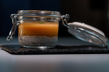 Elegant Glass Jar of Layered Chia Seed Pudding with Vibrant Mango Puree on Slate Board in Moody Lighting for Healthy Eating Concept