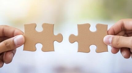 Two hands holding puzzle pieces, symbolizing collaboration, connection, and problem-solving in a bright, blurred background.