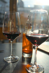Two wine glasses with red wine and a bottle with chili oil on a table in a restaurant in backlight with reflections