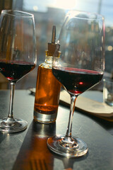 Two wine glasses with red wine and a bottle with chili oil on a table in a restaurant in backlight with reflections