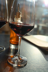 Two wine glasses with red wine and a bottle with chili oil on a table in a restaurant in backlight with reflections