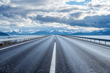 Empty asphalt road leading to snowy mountains in winter