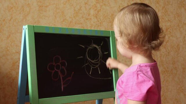 A small child draws with chalk on a blackboard. The child learns to write. Children's education
