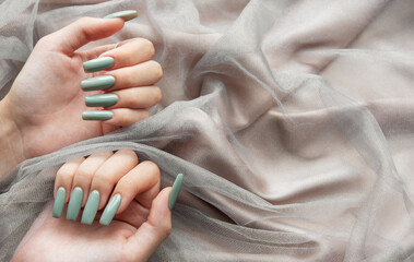 Elegant green manicure displayed on softly draped fabric with hands positioned artistically