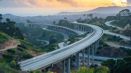 Obraz premium Aerial view of a winding elevated highway stretching through hilly, green terrain at sunset, surrounded by lush vegetation.
