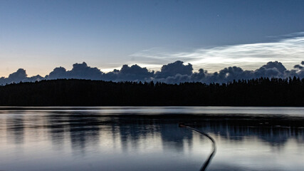 charming night landscape with silver clouds, silver clouds over the lake, dark forest silhouette in the background, mesospheric clouds