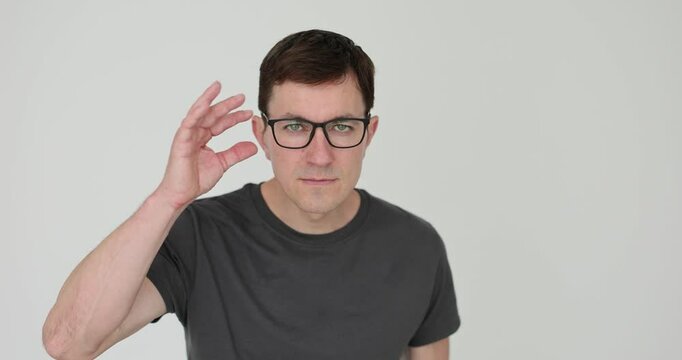 Strict man adjusts eyeglasses trying to see details on white background. Young guy with serious facial expression squints expressing attention