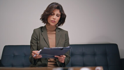 Corporate worker holding clipboard on office sofa closeup. Woman filling papers 