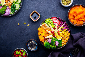 Vegan buddha bowl for balanced diet with sweet potato, quinoa, chickpeas, edamame, tofu, corn, radish, broccoli and seeds, black background, top view