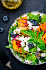 Foodie food salad with grilled peaches, blueberries, red onion, feta cheese, basil and arugula on black background, top view