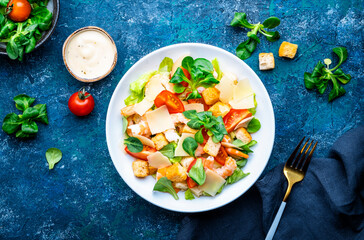 Caesar salad with shrimp, tomatoes, iceberg lettuce, croutons, parmesan cheese and classic dressing. Blue background, top view