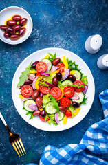 Vegan salad with olives, tomatoes, paprika, cucumber, lettuce and onion. Blue background, top view
