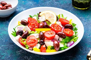 Greek salad with feta cheese, olives, tomatoes, lettuce, paprika, cucumber and onion. Blue background, top view