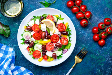 Greek salad with feta cheese, olives, tomatoes, lettuce, paprika, cucumber and onion. Blue background, top view