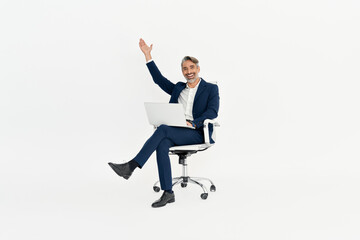 Happy mid adult business man using laptop celebrating success in office chair. Excited mature...