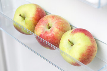 Apples in fridge. Isolated on white fridge door. Fresh green and red apples with small natural spots. Ripe bunch of apples on a transparent refrigerator shelf and in a plastic fridge drawer.