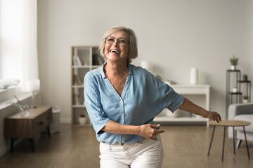Cheerful elderly woman in casual clothes dancing in living room, moving lively to favourite music, enjoy carefree retirement, good health, active lifestyle. Healthcare, vitality, good quality of life