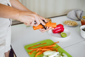 Peeling carrots in a bright kitchen while preparing a healthy meal with fresh vegetables and spices