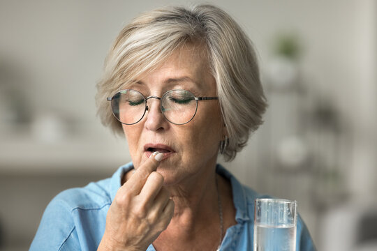 Close up old woman hold pill and glass of water, takes meds, maintain health, manage chronic pain or arthritis, take calcium, vitamin to prevent osteoporosis, lower cholesterol level, caring of health