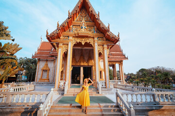 Travel by Asia . Young woman in hat and yellow dress walking near the Chalong buddhist temple on...